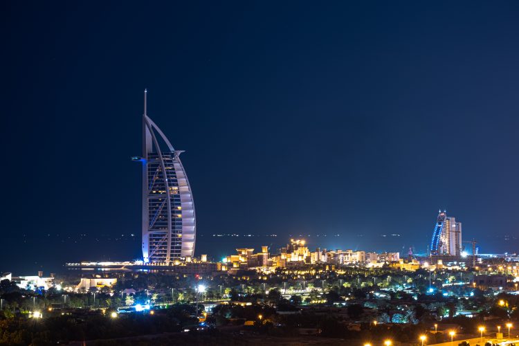 Burj Al Arab, a luxury hotel located in Dubai with its iconic sail-shaped structure and a backdrop of clear blue sky and sea.
