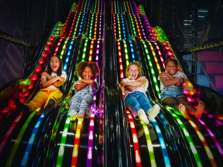 Two kids, a boy and a girl, jumping and playing on neon trampolines at the indoor play park in Dubai Parks and Resorts, surrounded by colorful neon lights
